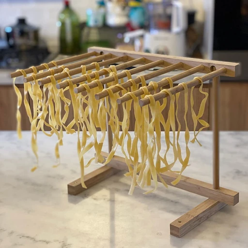 Pasta drying on a pasta drying rack on a marble top with kitchen in background.