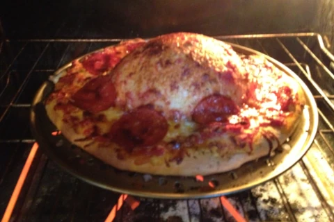 Pizza in oven forming a large bubble in the middle of the dough.